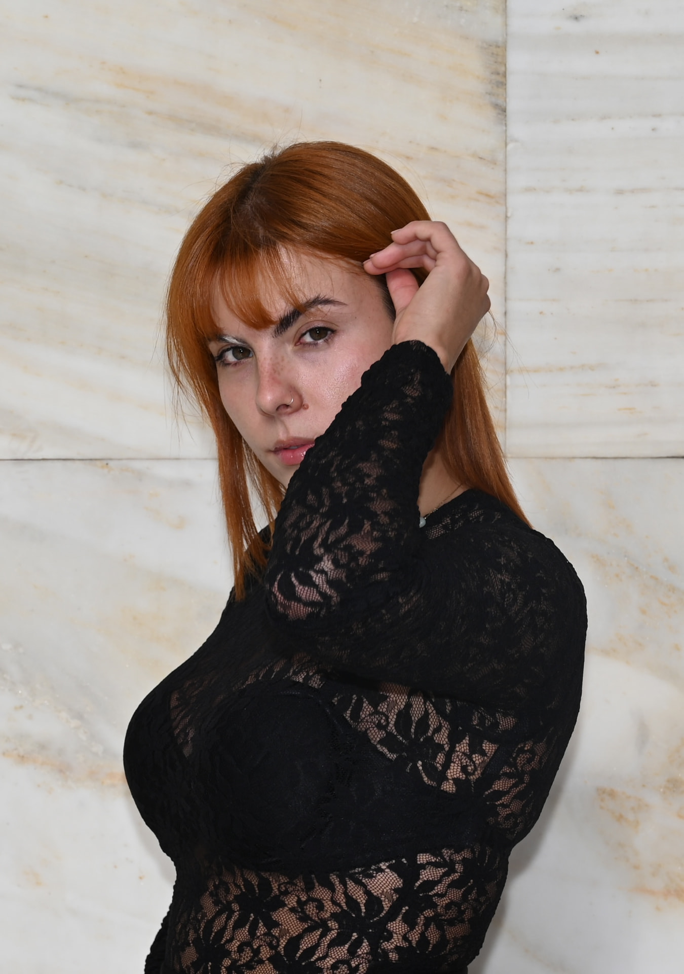 Musician in a black lace top photographed against a marble wall