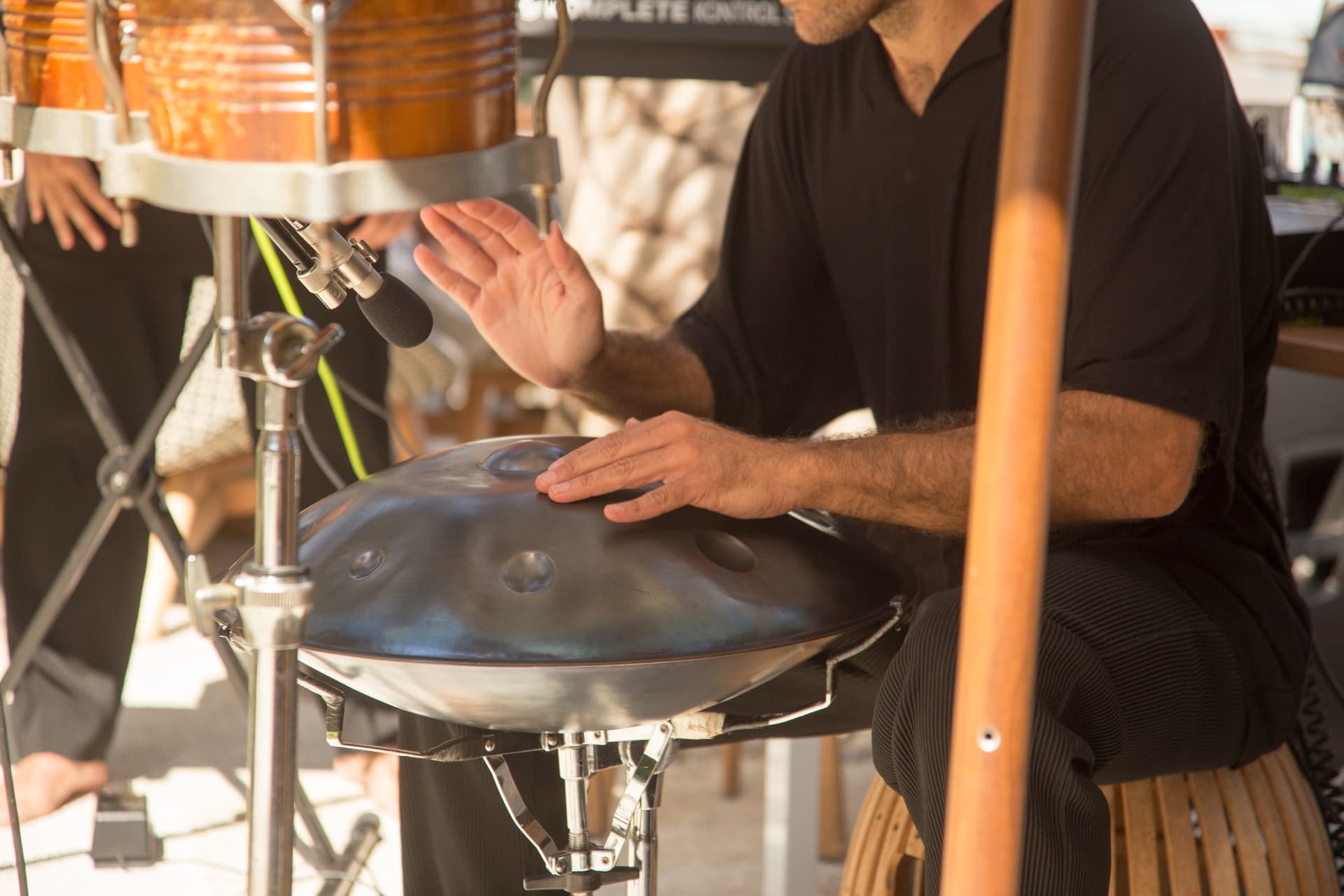 Handpan player's hands over the steel handpan on a sunlit terrace
