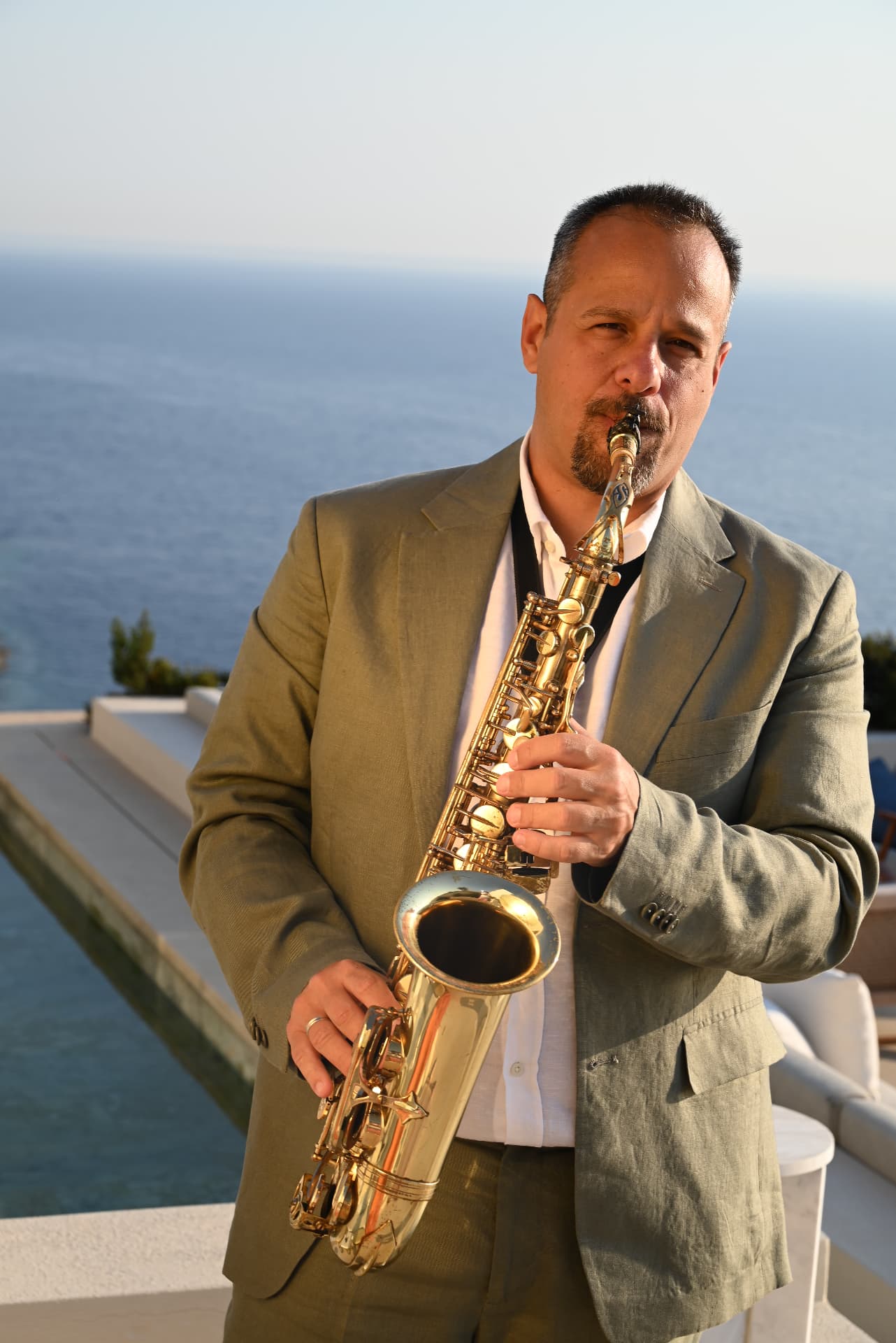Saxophonist in an olive suit with the sea behind him