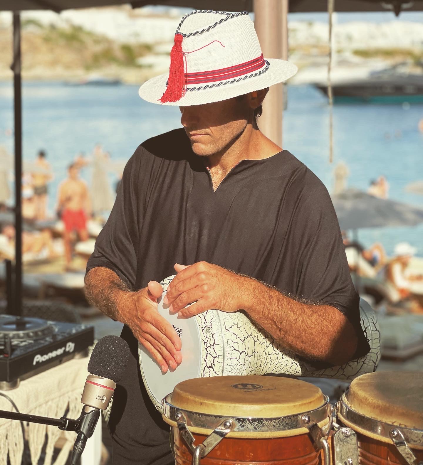 Percussionist in a white hat playing darbuka and congas by the sea