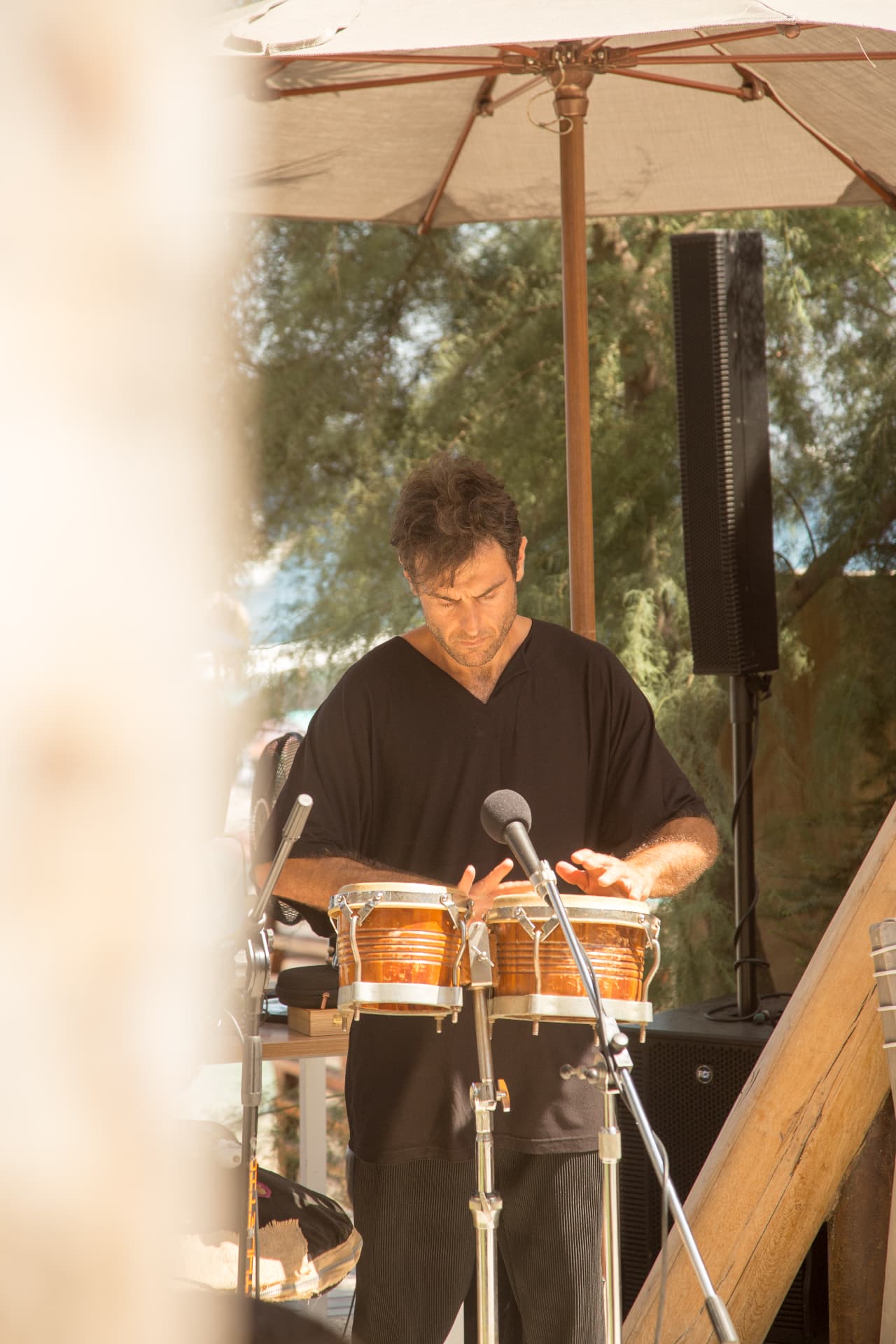 Percussionist playing the bongos beneath a parasol