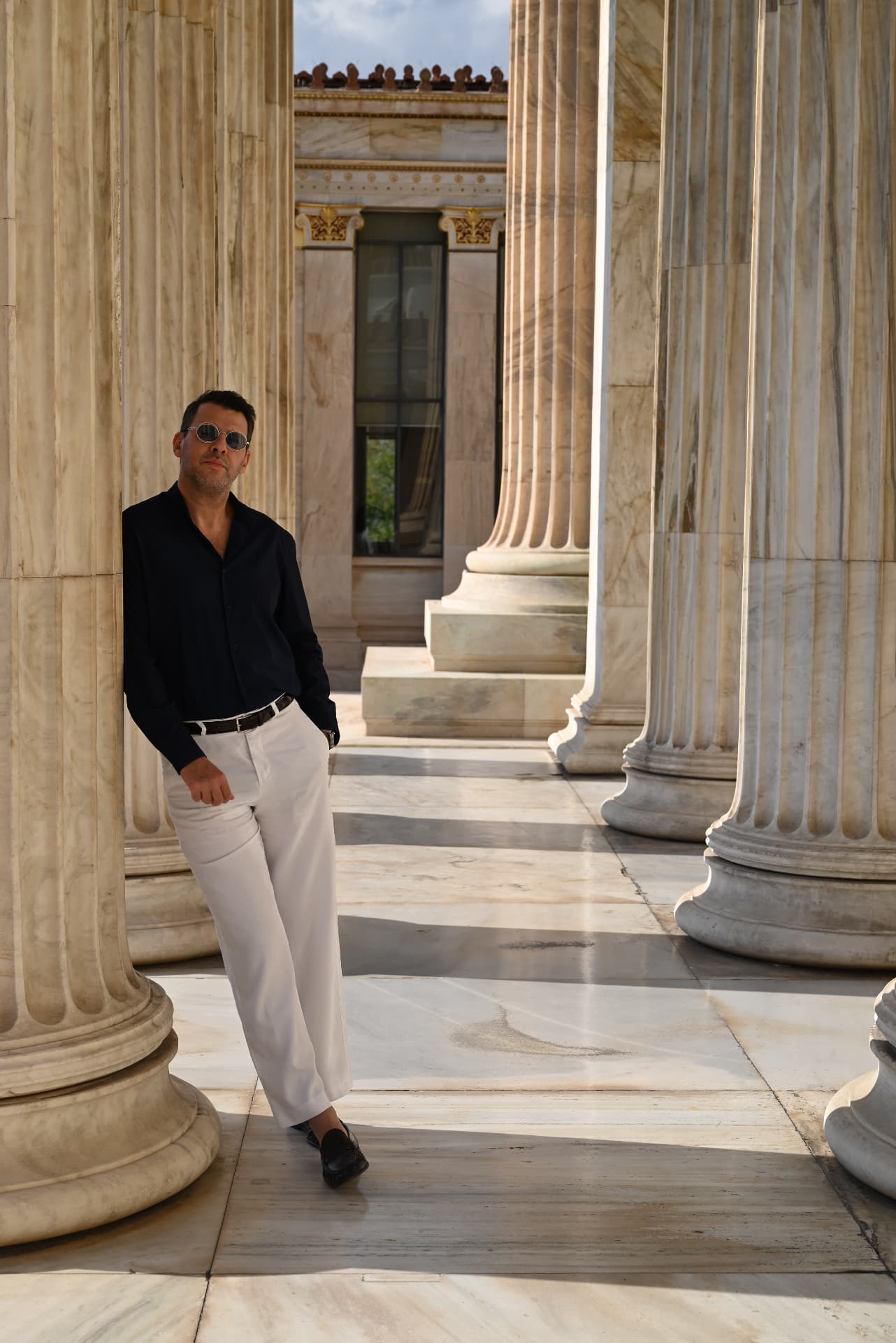 Constantin Nasiri standing among the marble columns of the Athens Academy