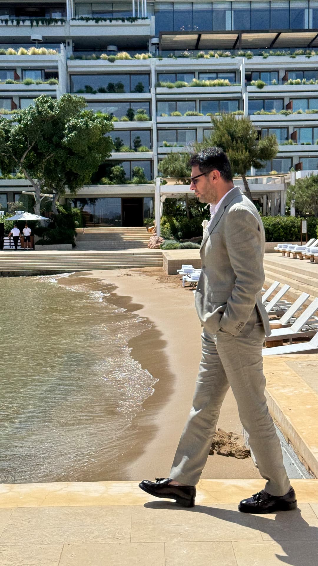 Constantin Nasiri in a linen suit walking along a hotel beach