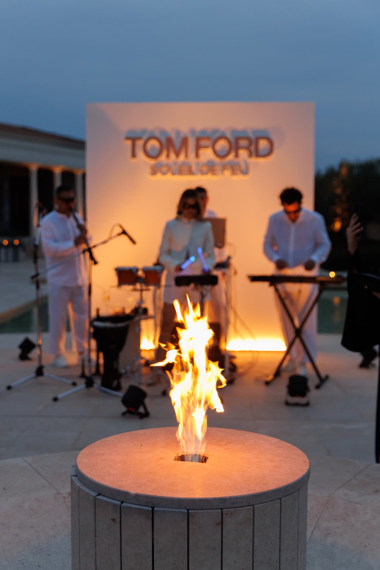 The band in white performing beside a fire bowl