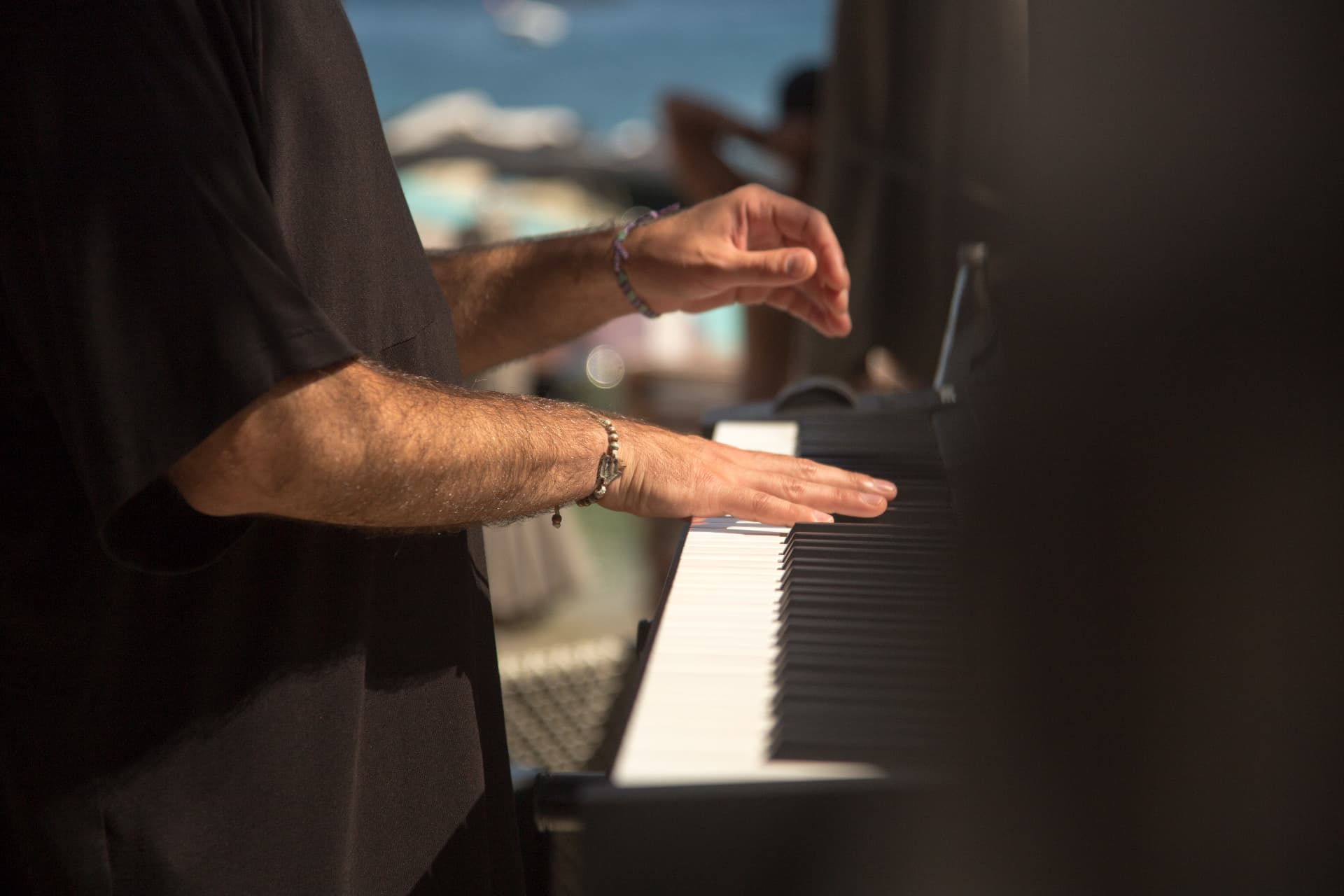 Keyboardist's hands over the piano keys with the Mykonos sea behind