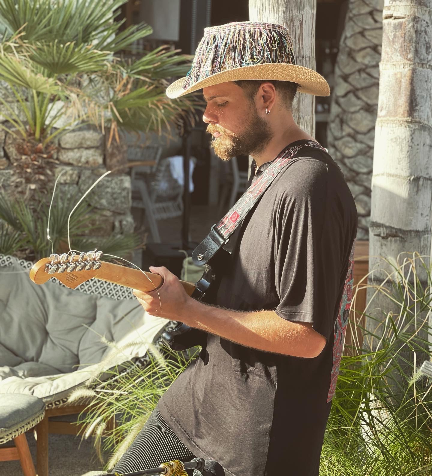 Guitarist in a fringed straw hat playing electric guitar among palms