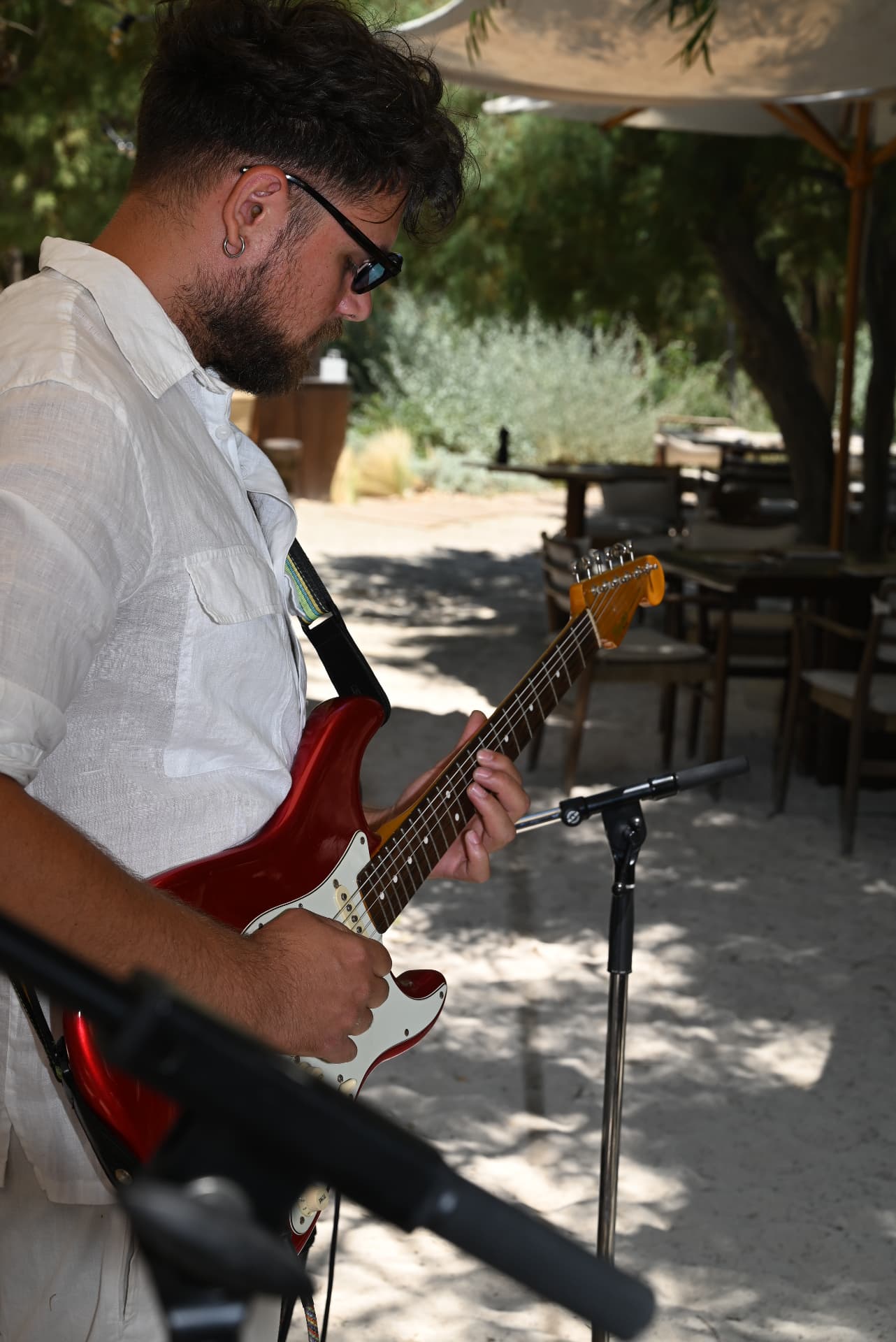 Guitarist in a white linen shirt playing a red electric guitar at an outdoor beach club